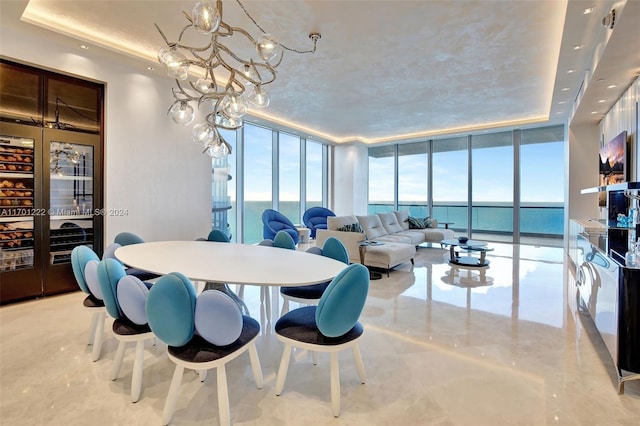 dining space with a notable chandelier, expansive windows, a water view, and a tray ceiling