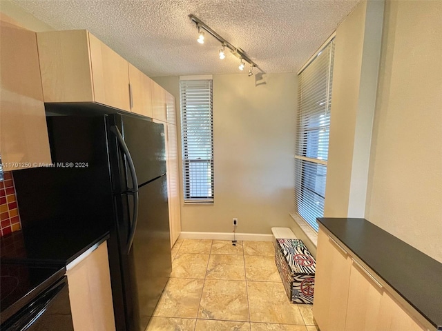 kitchen with light brown cabinets, black fridge, rail lighting, light tile patterned floors, and a textured ceiling