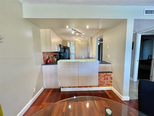 kitchen with decorative backsplash, track lighting, black fridge, a textured ceiling, and dark hardwood / wood-style floors