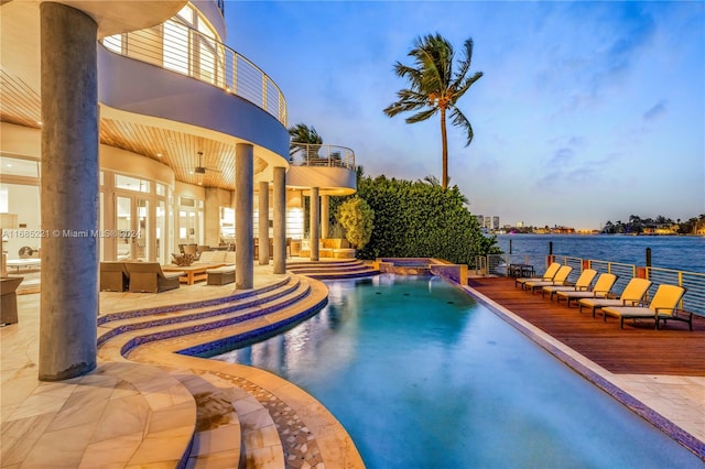 pool at dusk featuring a patio area, an outdoor living space, a water view, and pool water feature