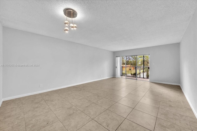 tiled spare room with a chandelier and a textured ceiling