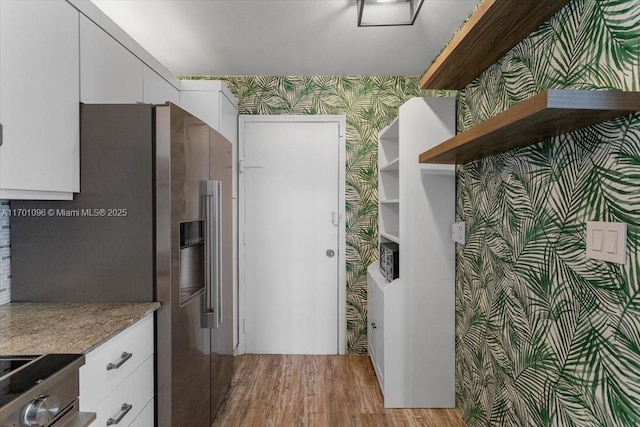 kitchen with stainless steel refrigerator with ice dispenser, range, light hardwood / wood-style floors, and white cabinets