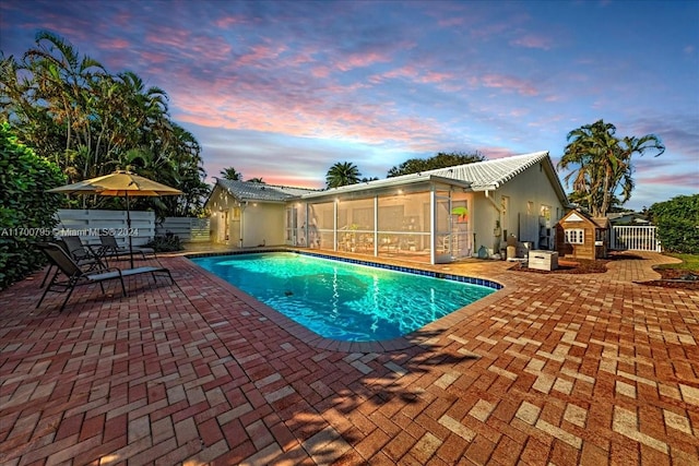 pool at dusk featuring a sunroom and a patio area