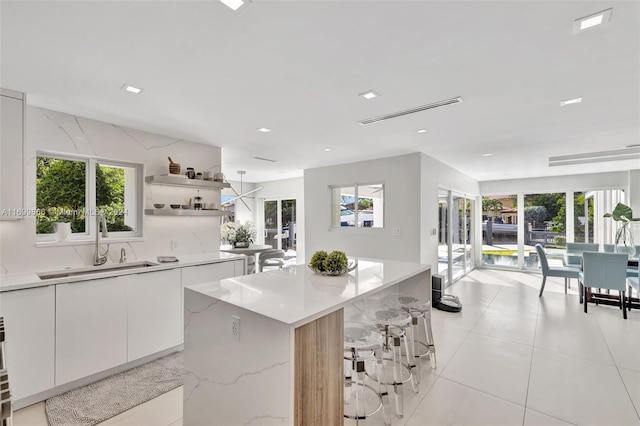 kitchen with a kitchen bar, sink, white cabinetry, light stone counters, and a center island