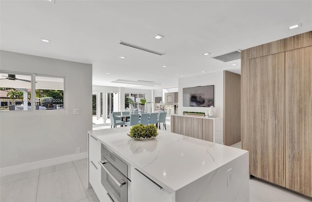 kitchen with light tile patterned floors, a center island, light stone counters, white cabinets, and stainless steel oven