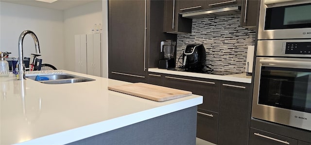 kitchen featuring under cabinet range hood, stainless steel appliances, a sink, light countertops, and backsplash