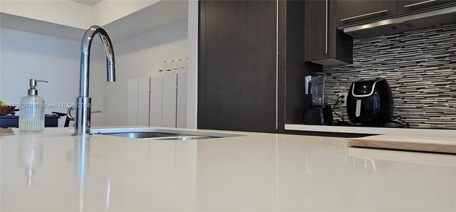 kitchen with decorative backsplash, light countertops, dark brown cabinets, under cabinet range hood, and a sink