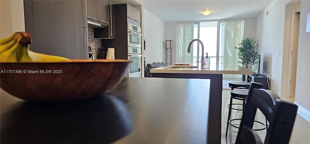 kitchen with double oven, a breakfast bar, a sink, expansive windows, and an island with sink