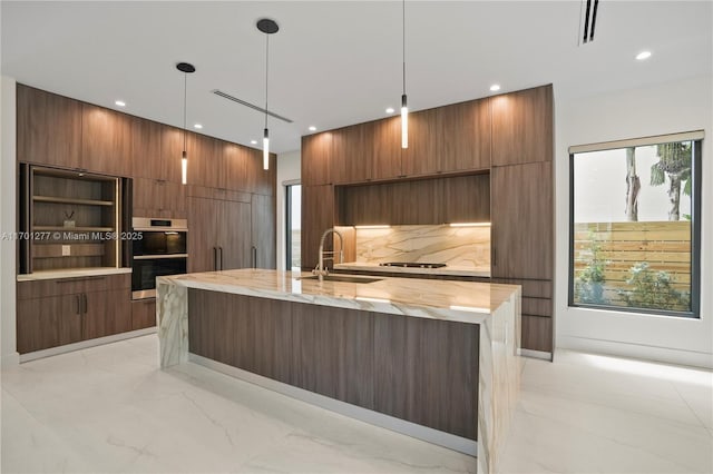 kitchen featuring stainless steel double oven, modern cabinets, a center island with sink, and a sink