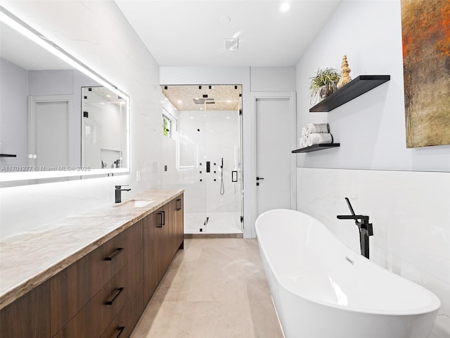 bathroom with a freestanding bath, a shower stall, vanity, and tile walls