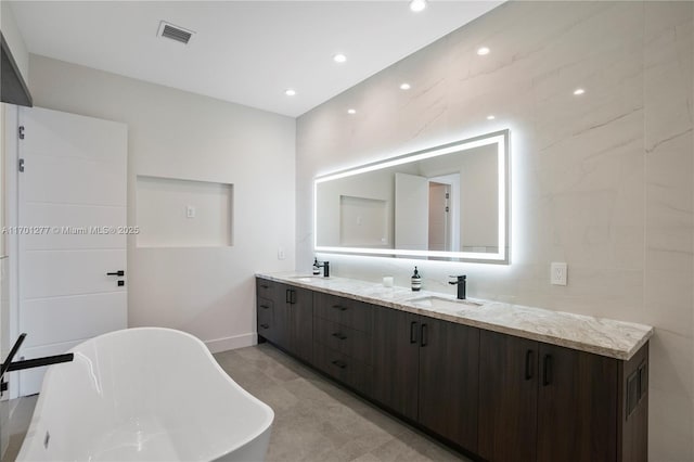 bathroom featuring a sink, double vanity, visible vents, and a soaking tub