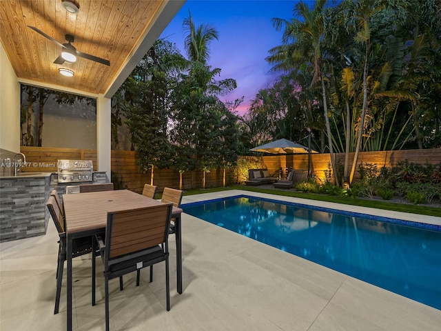 pool at dusk featuring area for grilling, an outdoor kitchen, a fenced backyard, and a patio area