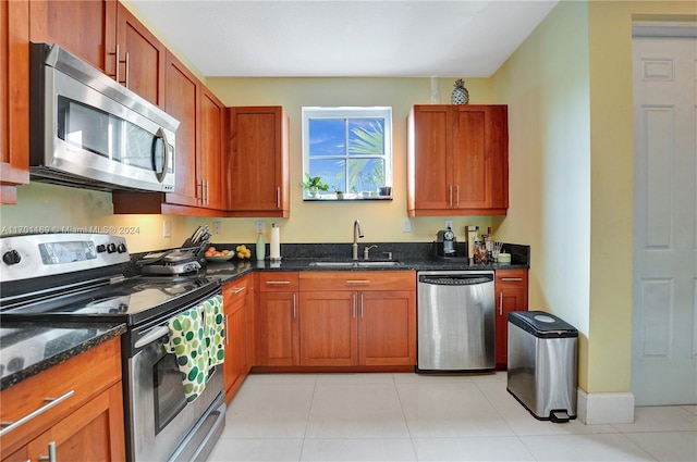 kitchen featuring sink, light tile patterned floors, dark stone counters, and appliances with stainless steel finishes