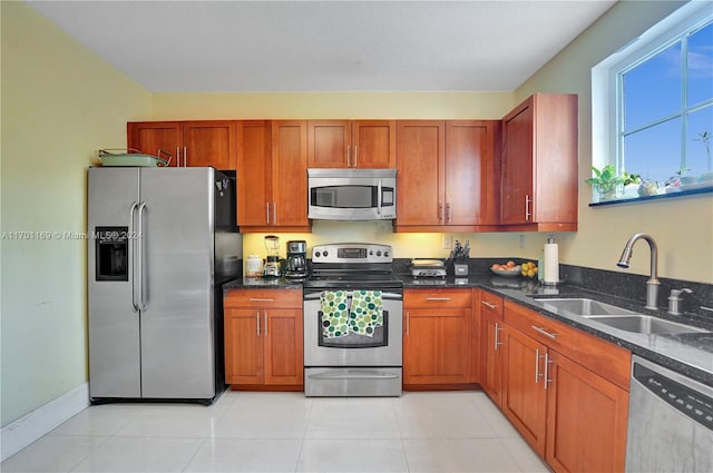 kitchen with appliances with stainless steel finishes, light tile patterned floors, dark stone counters, and sink