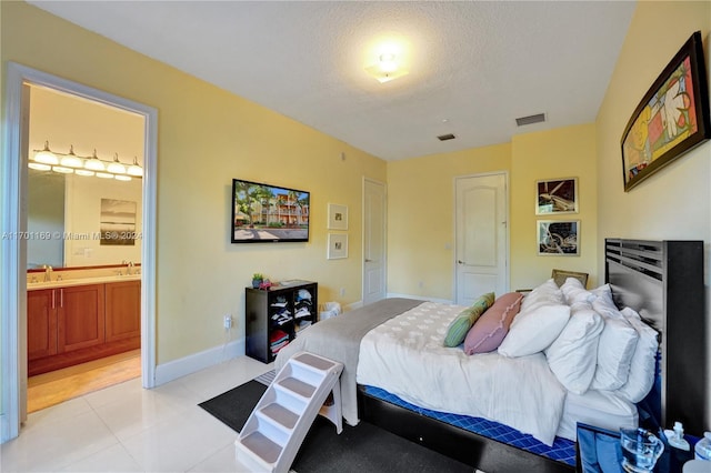 bedroom featuring connected bathroom, sink, light tile patterned floors, and a textured ceiling