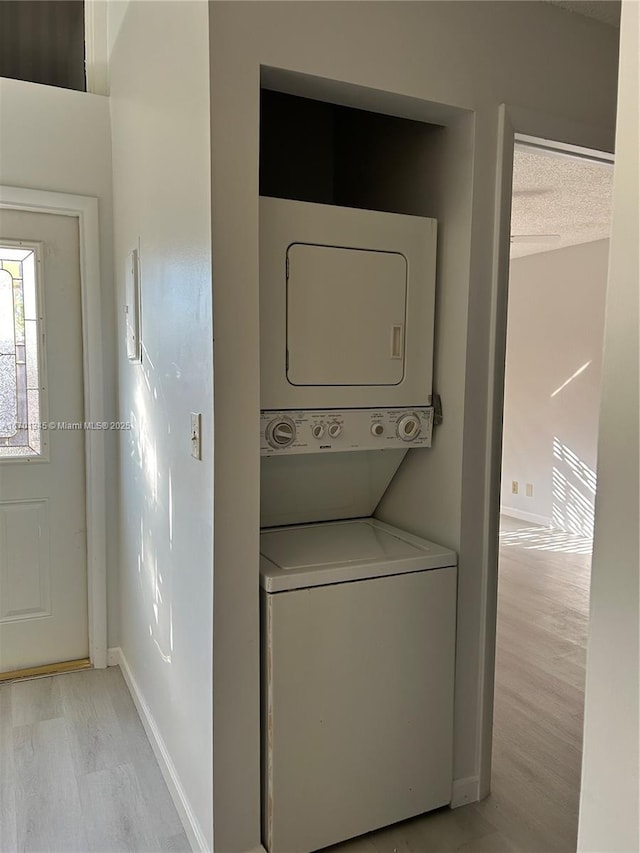 laundry room featuring stacked washer and dryer, a textured ceiling, and light wood-type flooring