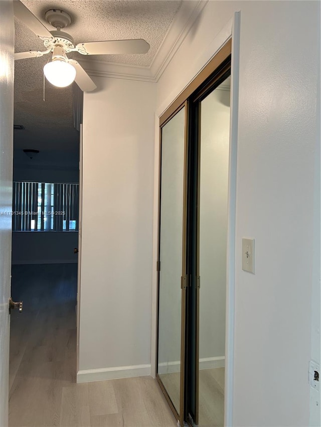 hallway featuring ornamental molding, a textured ceiling, and light wood-type flooring