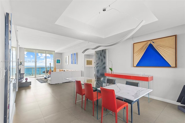 dining room with a raised ceiling, floor to ceiling windows, and a water view