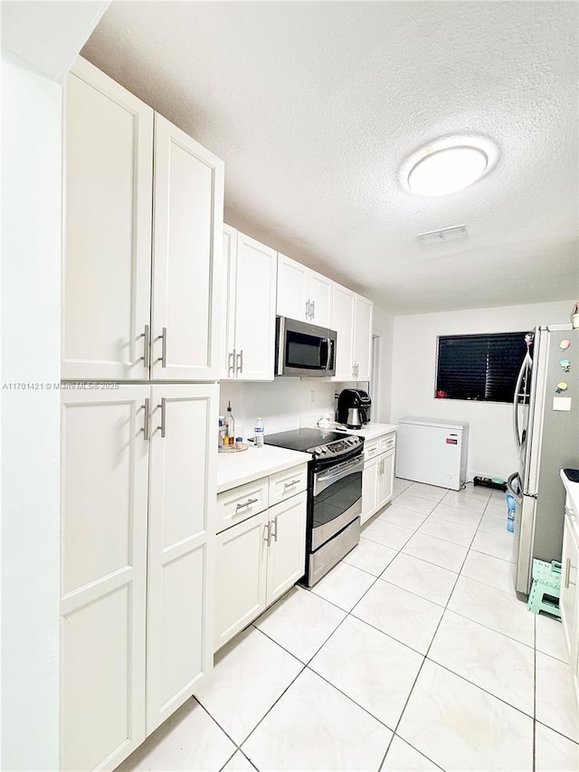 kitchen featuring white cabinetry, light tile patterned floors, stainless steel appliances, and a textured ceiling