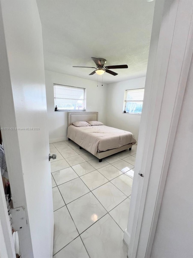 unfurnished bedroom with ceiling fan, multiple windows, and light tile patterned floors