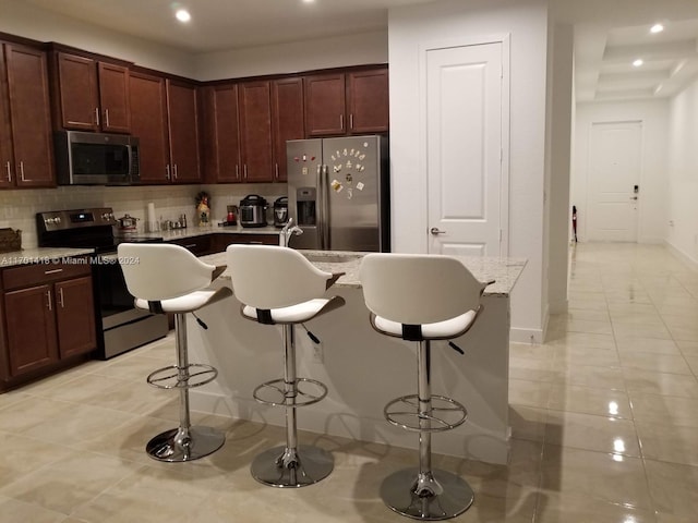 kitchen featuring a kitchen breakfast bar, stainless steel appliances, light tile patterned floors, and a kitchen island with sink