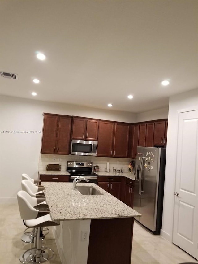 kitchen featuring light stone counters, sink, an island with sink, and appliances with stainless steel finishes