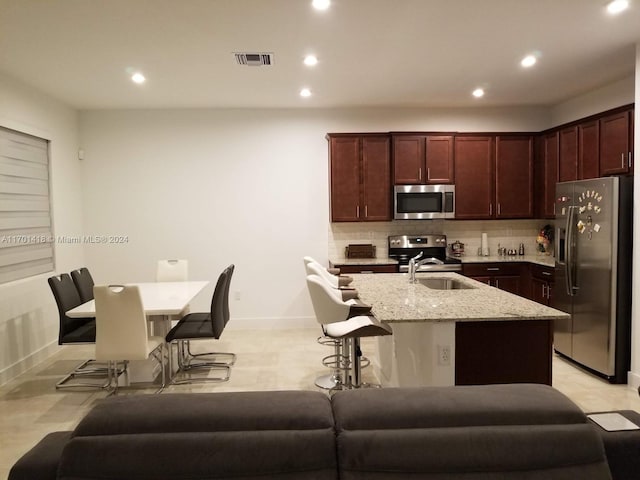 kitchen featuring light stone countertops, stainless steel appliances, a breakfast bar area, decorative backsplash, and a center island with sink