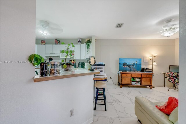 kitchen with a breakfast bar, kitchen peninsula, white cabinetry, and ceiling fan