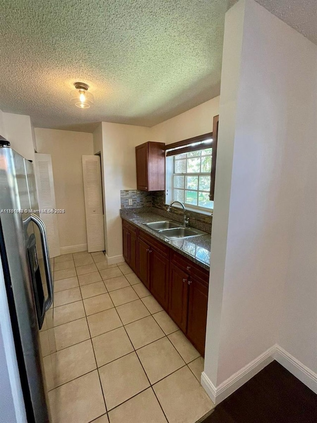 kitchen with stainless steel refrigerator, sink, backsplash, a textured ceiling, and light tile patterned flooring