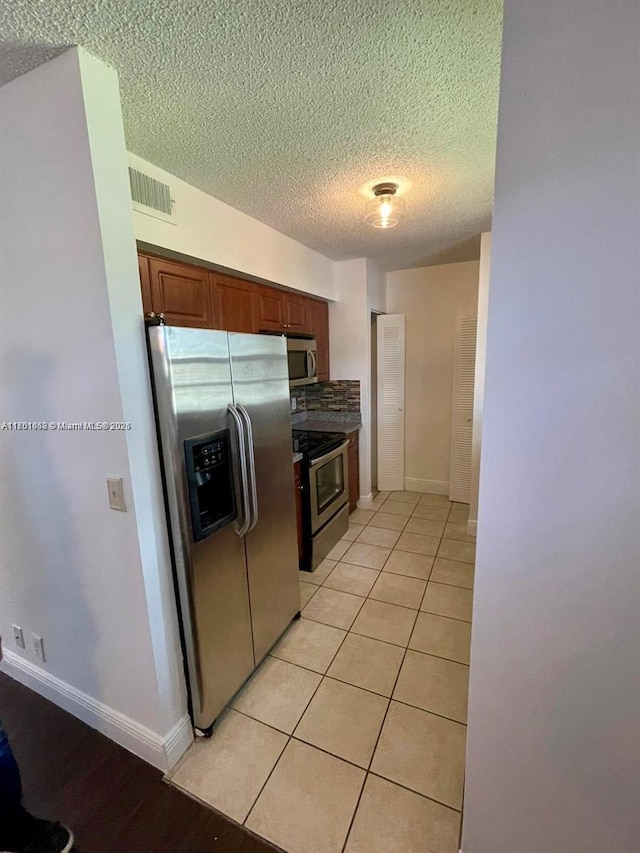 kitchen featuring stainless steel appliances, light tile patterned floors, and a textured ceiling