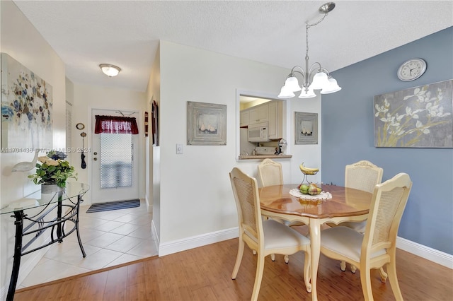 dining space with an inviting chandelier, a textured ceiling, and light hardwood / wood-style flooring