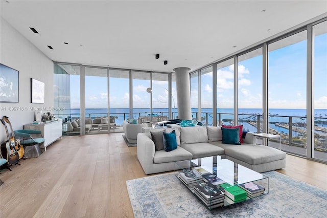 living room with floor to ceiling windows, a water view, and light hardwood / wood-style flooring