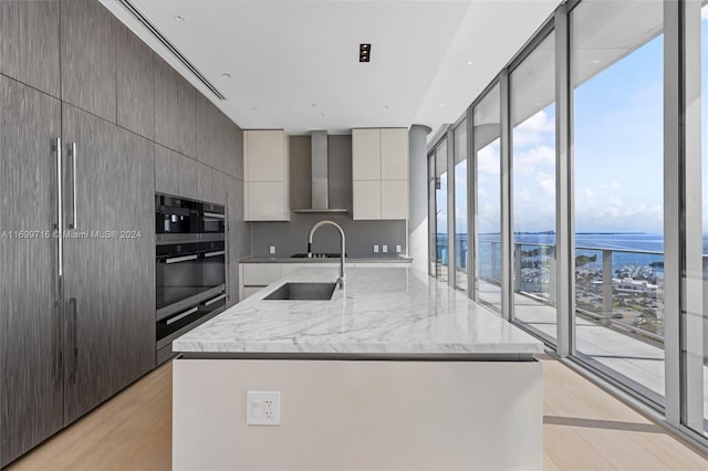 kitchen with wall chimney exhaust hood, plenty of natural light, and a kitchen island with sink