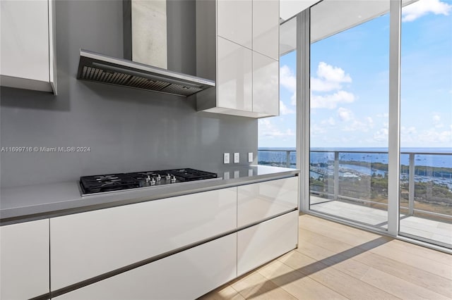 kitchen with a water view, wall chimney exhaust hood, white cabinets, and light wood-type flooring