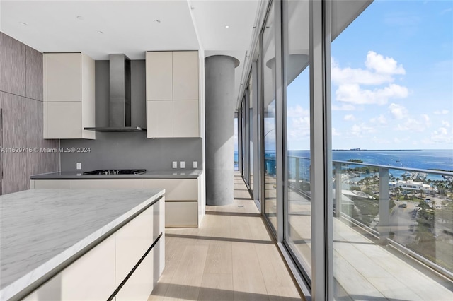 kitchen with light hardwood / wood-style floors, gas stovetop, wall chimney range hood, a water view, and gray cabinets