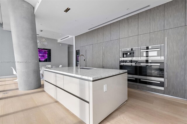 2675 S Bayshore Dr Unit 1602S, Miami, FL 33133 - kitchen with a sink, double oven, a warming drawer, light wood-type flooring, and light stone countertops
