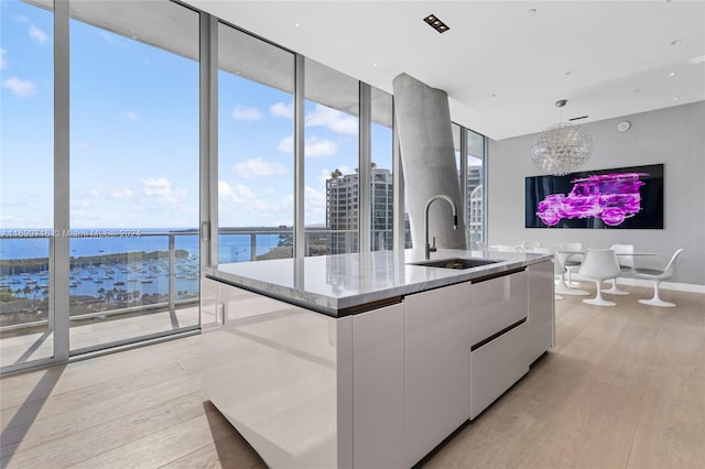 kitchen with light wood-type flooring, sink, pendant lighting, a water view, and white cabinets