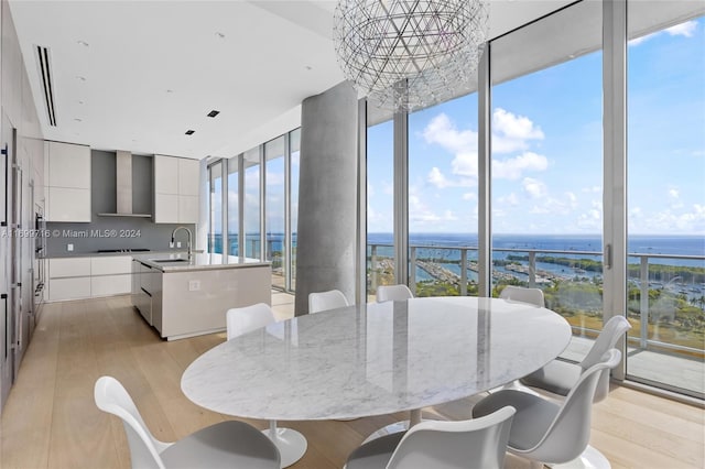 dining space with light hardwood / wood-style flooring, a water view, a healthy amount of sunlight, and a notable chandelier