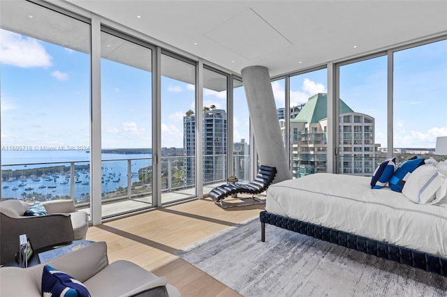 bedroom featuring hardwood / wood-style flooring, a water view, and a wall of windows