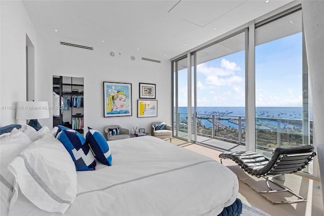 bedroom with access to exterior, expansive windows, a water view, and light hardwood / wood-style floors