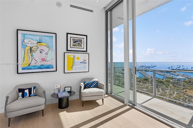 sitting room featuring expansive windows, light hardwood / wood-style flooring, and a water view