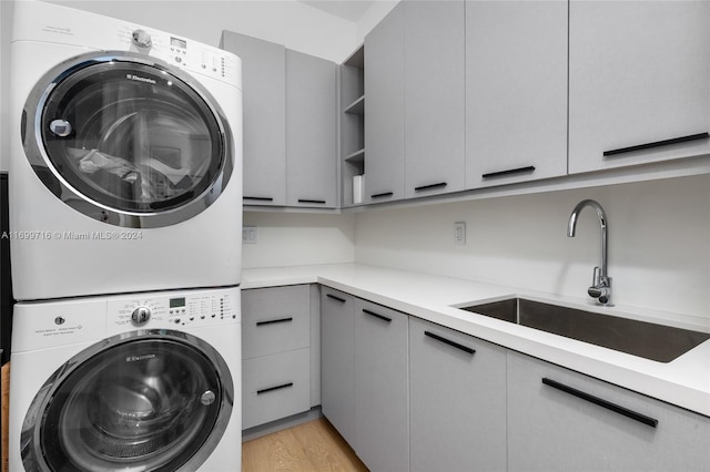 clothes washing area with cabinets, light wood-type flooring, sink, and stacked washer and clothes dryer