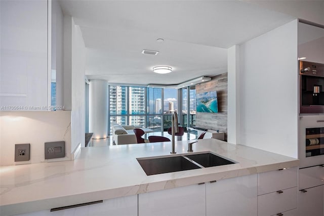 kitchen with white cabinetry, sink, light stone counters, expansive windows, and oven