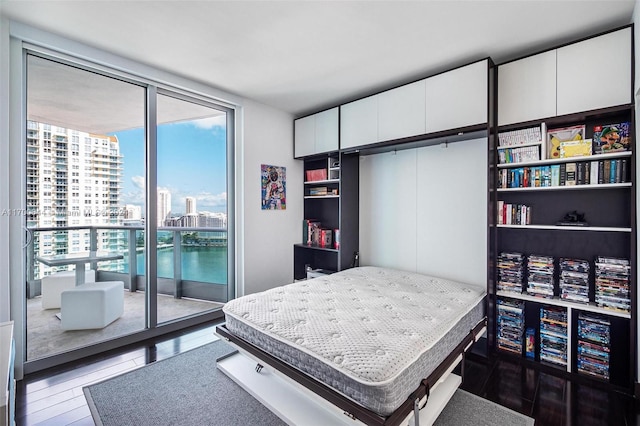 bedroom with access to exterior, a water view, expansive windows, and dark wood-type flooring