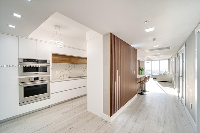 kitchen featuring white cabinetry, stainless steel double oven, hanging light fixtures, tasteful backsplash, and light hardwood / wood-style floors