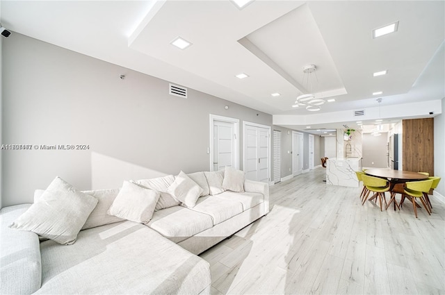 living room with light wood-type flooring and a raised ceiling