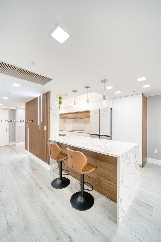 kitchen featuring light wood-type flooring, pendant lighting, white refrigerator, and light stone counters