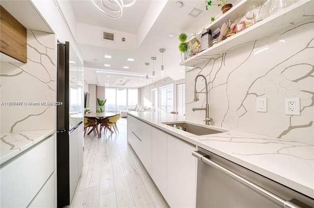 kitchen featuring sink, hanging light fixtures, light hardwood / wood-style flooring, light stone counters, and stainless steel appliances