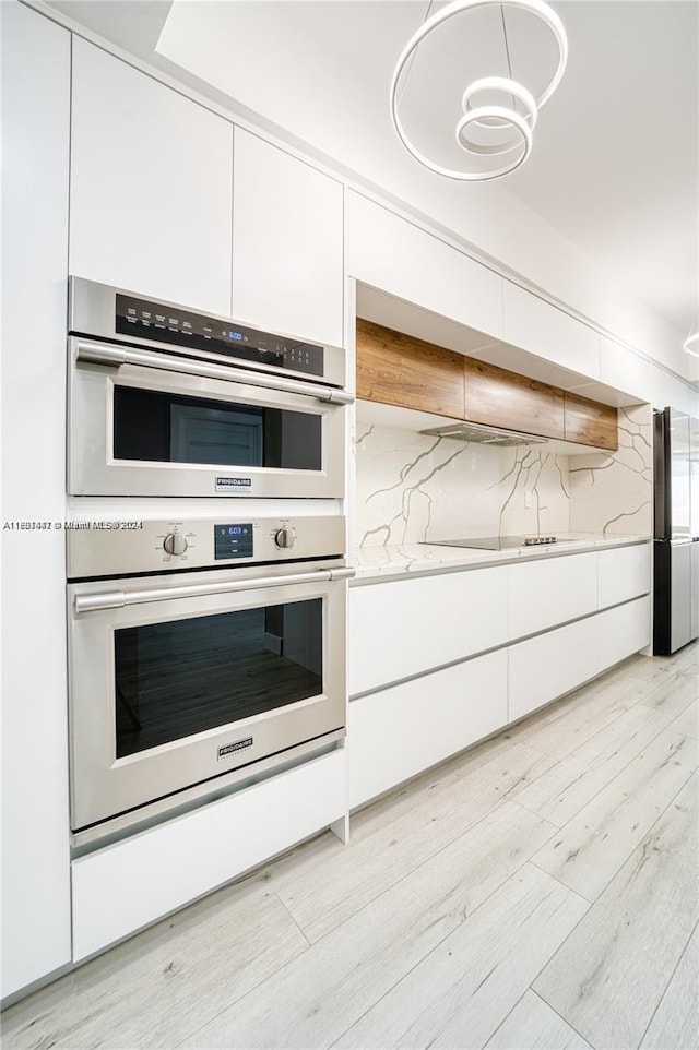 kitchen featuring light hardwood / wood-style flooring, tasteful backsplash, white cabinetry, light stone counters, and stainless steel double oven