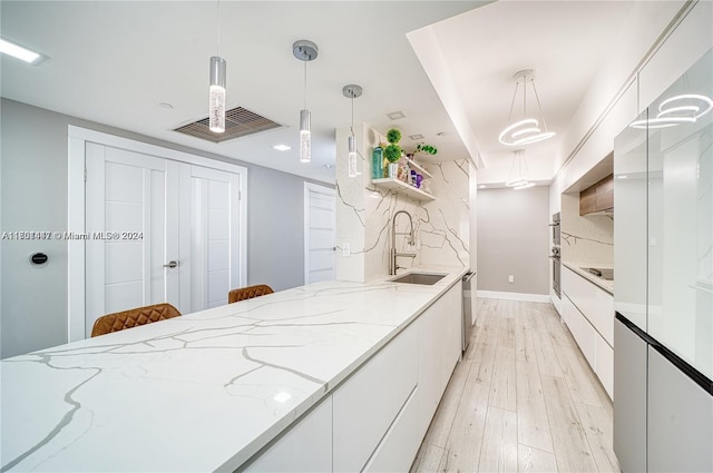 kitchen with white cabinets, pendant lighting, light wood-type flooring, and light stone counters